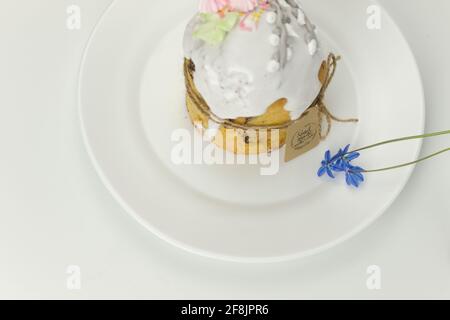 Orthodox Easter cake with white fondant tied with a rope with tag on a plate with spring flowers in a pot side view Stock Photo