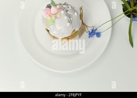 Orthodox Easter cake with white fondant and marshmallows tied with a rope on a plate with spring flowers in a pot top view Stock Photo