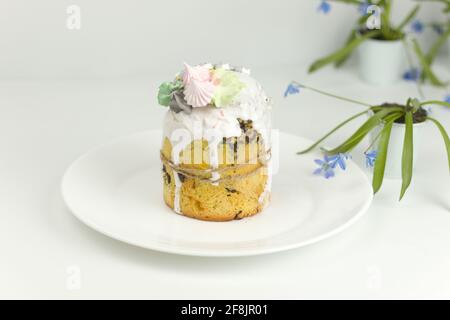 Orthodox Easter cake with white fondant and marshmallows tied with a rope on a plate with spring flowers in a pot, side view Stock Photo