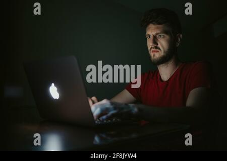 BRCKO, BOSNIA AND HERZEGOVINA - May 02, 2020: Man using Macbook laptop in dark ro Stock Photo