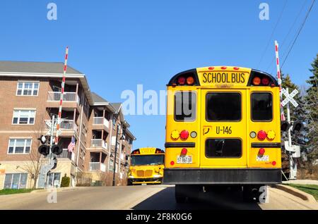 South Elgin, Illinois, USA. School buses going in opposite directions stopped, as required by law, at a railroad crossing. Stock Photo