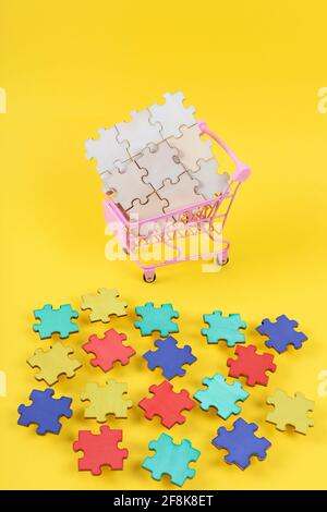 World Autism Aawareness Day background. Shopping trolley with different color pieces of jigsaw puzzle on yellow background. Stock Photo