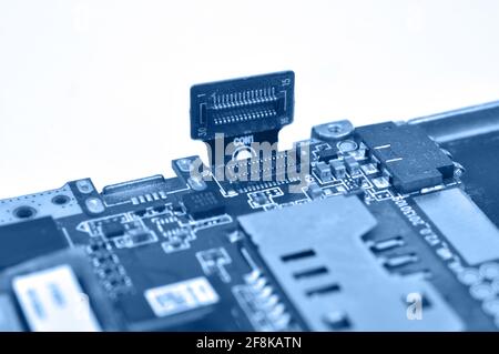 Disassembled mobile phone or smartphone. Circuit board and cable plume. Macro photo in blue tone. Stock Photo