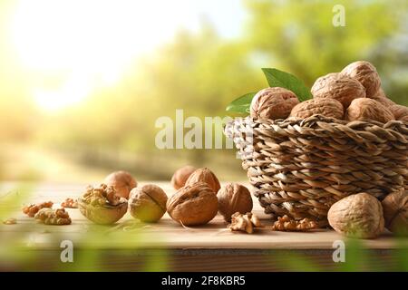 Basket full of walnuts on a table with split walnuts with seeds in sight on wooden table in a field of walnut trees. Stock Photo