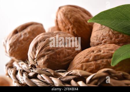 Detail of wicker basket full of walnuts with leaves and white isolated background. Front view. Stock Photo