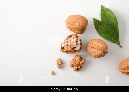 Walnuts in shell and broken showing seeds with leaves on white table. Top view. Stock Photo
