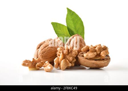 Walnuts in shell and broken showing seeds with leaves on white table and white isolated background. Front view. Stock Photo