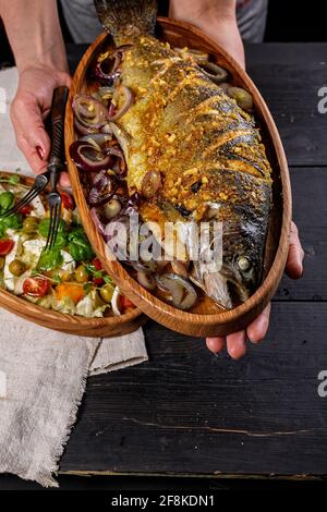 Seafood and vegetable salad. Delicious and healthy lunch. Female hands hold a wooden dish with grilled fish. Mediterranean diet. Vertical shot. Food p Stock Photo