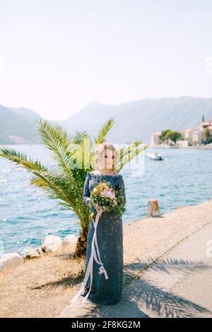 The bride in a stylish gray dress stands with wedding bouquets on the pier near old town of Perast Stock Photo