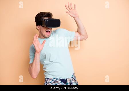 Portrait of nice terrified guy wearing vr helmet feeling fear exploring cyber space isolated over beige pastel color background Stock Photo