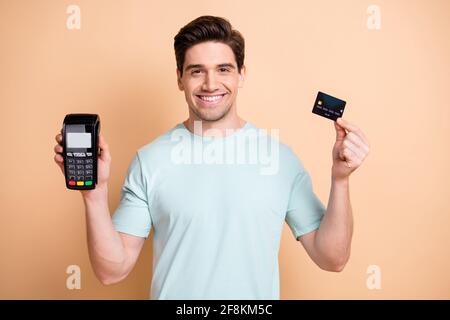 Portrait of nice cheerful guy holding in hands pos terminal bank card safe transaction isolated over beige pastel color background Stock Photo