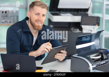 young technician using a tablet to fix a printer Stock Photo