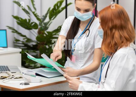 A doctor shows a redheaded nurse important test results. A 50-year-old woman in a wheelchair in a doctor's office. Stock Photo