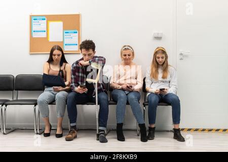 Patients sit in a clinic waiting for their turn to go to the doctor's office. They look at their cell phone while waiting. Stock Photo