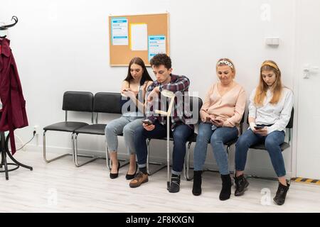 Patients sit in a clinic waiting for their turn to go to the doctor's office. They look at their cell phone while waiting. Stock Photo