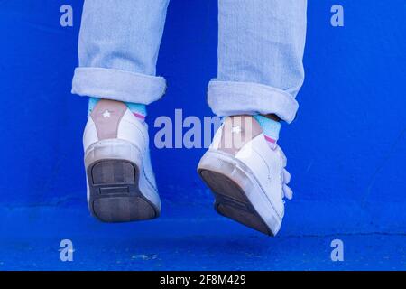 Close-up shot of a little girl's feet dangling from a blue wall. Stock Photo