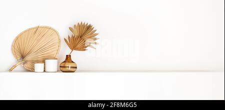 Header with coastal boho style interior decor, a brown glass vase with dried palm fans and a woven wall basket isolated on a white shelf Stock Photo