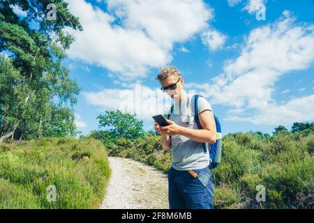 Young Male tourist with backpack using smartphone navigation app during hiking walk in the summer forest. Technology in everyday life. Local Traveling Stock Photo