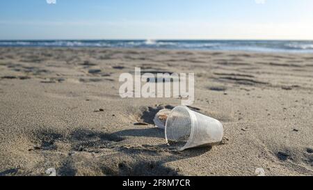 Disposable plastic glass discarded on sea coast ecosystem,nature waste pollution Stock Photo