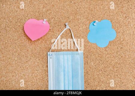 Cork board with pinned fase medical mask. Paper heart and flower shape sticky notes  in office concept Stock Photo