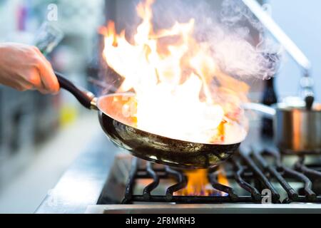 Chef in restaurant kitchen at stove with pan, doing flambe on food Stock Photo