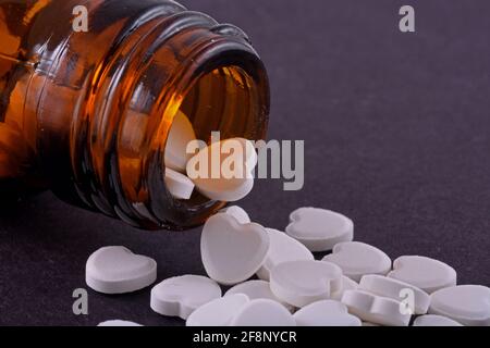 Heart shaped pills from bottle glass on a black background Medicines that help people Stock Photo