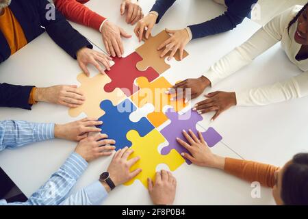 Office team assembling jigsaw puzzle pieces on table top view on hands Stock Photo