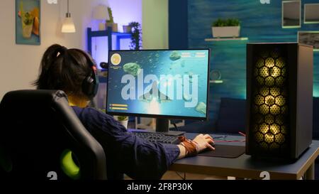 Back shot of focused cyber player wearing headset during space shooter championship. Pro gamer using RGB keyboard for online gaming competition late at night in living room Stock Photo