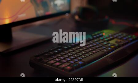 Close up of professional keyboard with RGB lighting prepared for streaming online tournament, display with first person shooter playing on it. Gaming studio of esport video game with powerful computer Stock Photo