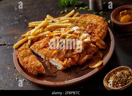 Closeup of yummy fried breaded pork escalope garnished with traditional aromatic chasseur sauce with mushrooms served with French fries on rustic wood Stock Photo
