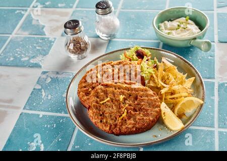 High angle of delicious fried fish cutlets on plate with fries and lettuce with fresh lemon served on table with sauce Stock Photo