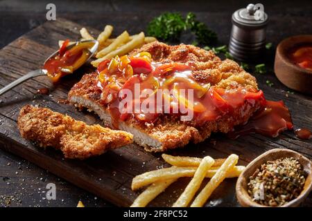 Closeup of delicious fried breaded meat Gypsy Schnitzel with spicy pepper sauce served with French fries as traditional German fast food Stock Photo