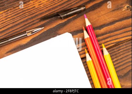 Colorful pencils, ballpoint pens, and white sheets of paper on a wooden table. Close-up selective focus. Stock Photo