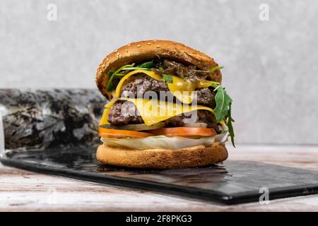 Double Beef Burger on design plate with grey background. Ingredients Bread, Cheddar cheese, Double Beef pattie, Vegetables,  lettuce, Sauce Stock Photo