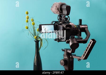 The camera on the gimbal shoots flowers in a vase. Turquoise background.