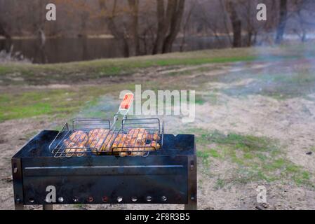 barbecue in nature in the spring. a man's hand holds a grate of meat over the coals. Stock Photo