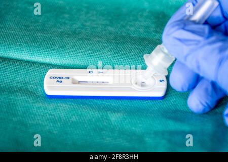 Close up of health care worker wearing blue surgical gloves and placing the sample in the covid-19 antigen diagnostic drug on a green surgical fabric Stock Photo