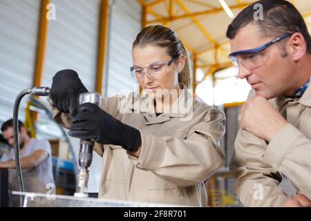 engineer showing female apprentice how to use drill in factory Stock Photo