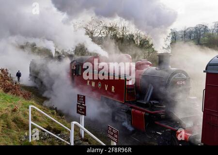 Historic steam trains (locos) puffing dramatic smoke clouds stopped at crossing (engine driver in cab) - heritage railway, KWVR, Yorkshire England UK. Stock Photo