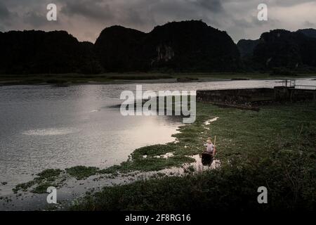 Beautiful landscape with fishing person in Van Long Nature Reserve, Tam Coc, Ninh Binh in Vietnam. Rural scenery photo from the boat taken in south ea Stock Photo