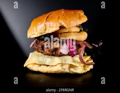 A Burger with onion rings against a dark background Stock Photo