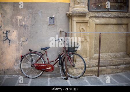 Red Bicycle with Basket, Locked Up Leaning against a wall in Florence, Italy Stock Photo