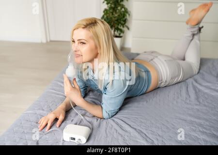 Young woman doing inhalation with inhaler at home. girl inhales medicine through a nebulizer mask. treatment of the respiratory tract Stock Photo