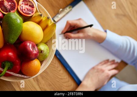 Nutritionist, dietitian woman writing a diet plan, with healthy vegetables and fruits, healthcare and diet concept. Female nutritionist with fruits wo Stock Photo