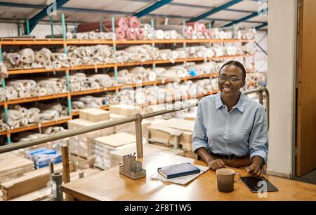 Smiling young African woman sitting at her desk in a warehouse Stock Photo