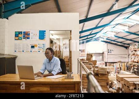 Young African woman working on a laptop at her warehouse desk Stock Photo