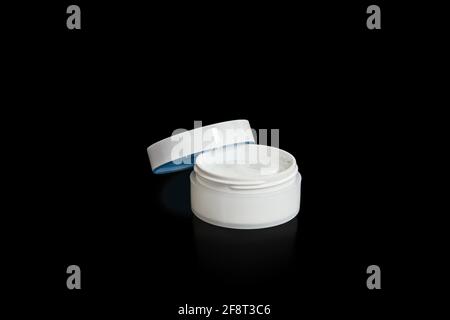 Cosmetic jar with face cream on black background. Opened blank white cosmetic container. Facial care concept Stock Photo