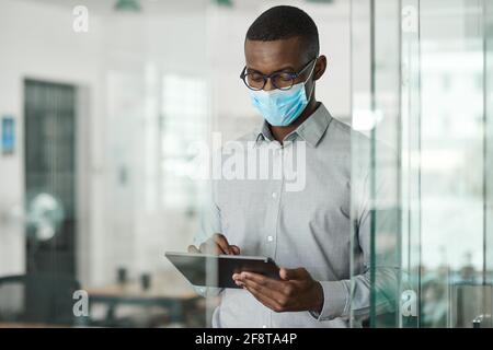 African businessman in a face mask using a tablet at work Stock Photo
