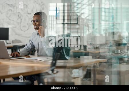 Smiling African businessman using a laptop and talking on a headset Stock Photo