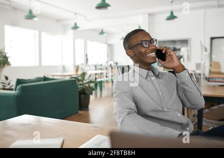 Smiling young African businessman talking on his phone at work Stock Photo